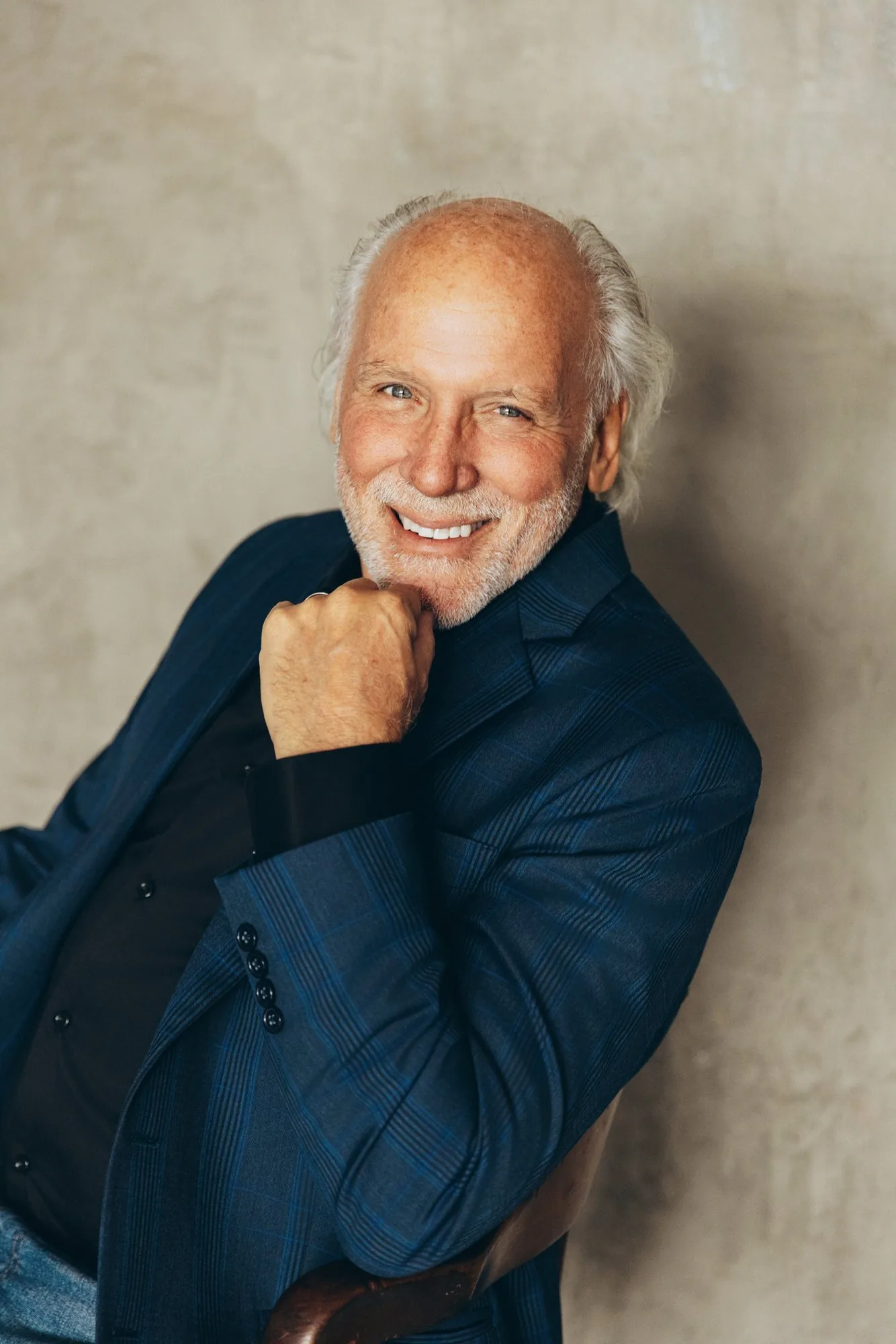 Dennis DiNoia in a navy blazer, hand on chin, smiling