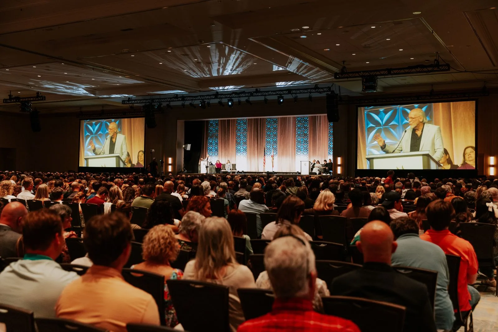 A packed convention hall watching Dennis on the big screens